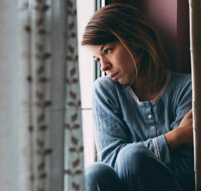 woman looking outside the window looking sad and depressed