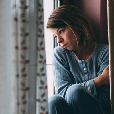 woman looking outside the window looking sad and depressed