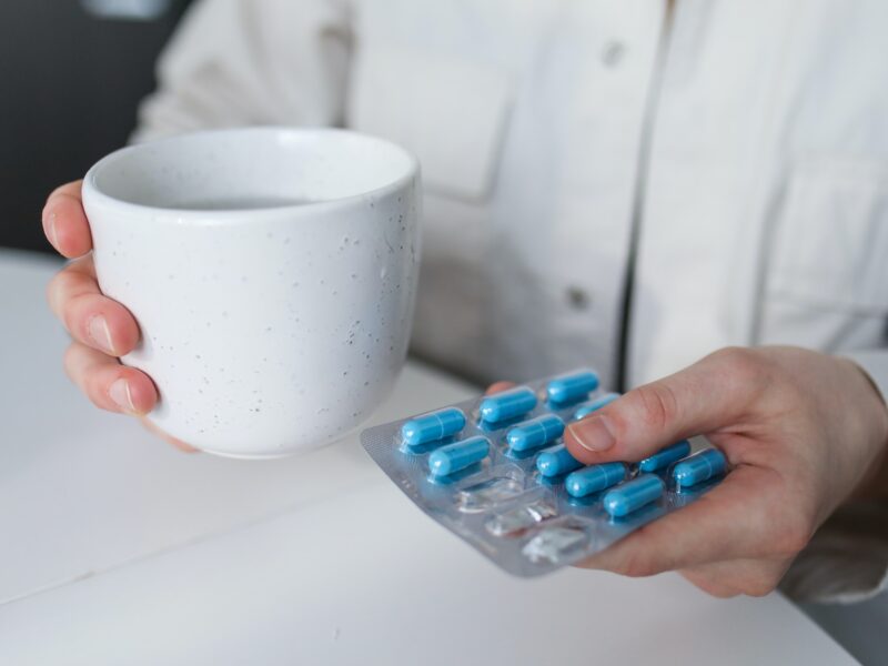 man holding a cup and a pack of blue pills