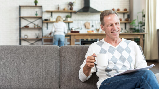 Man sitting on a couch reading with a coffee mug in a living room