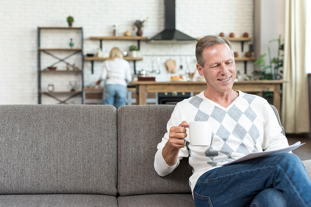 Man sitting on a couch reading with a coffee mug in a living room