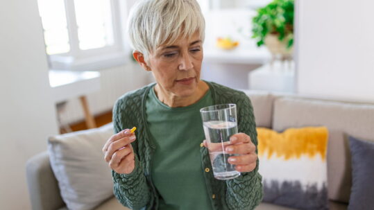senior woman takes pill with glass water hand