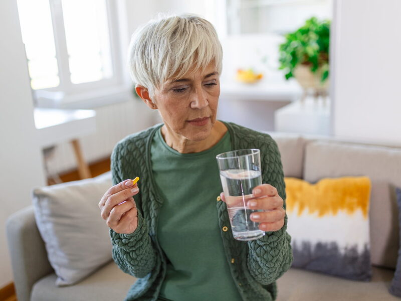 senior woman takes pill with glass water hand