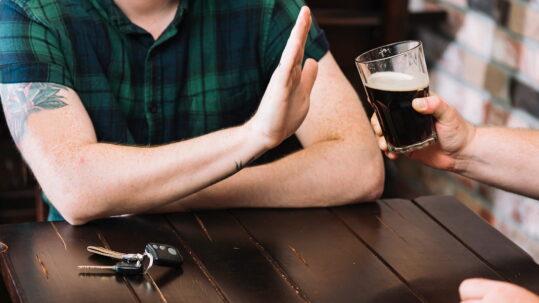 Man refusing glass of rum offered by his friend.